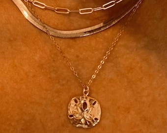 Può includere: Una collana d'oro con tre catene e un ciondolo a forma di dollaro di sabbia.