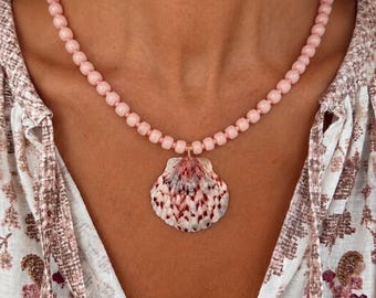 Può includere: Una delicata collana con una fila di piccole perline rosa chiaro. La collana ha un ciondolo a forma di conchiglia con una base bianca e intricati motivi rossi e marroni. Un bellissimo gioiello.