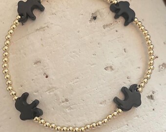 May include: Gold beaded bracelet featuring four black elephant charms. The bracelet is made of small, round gold beads strung together, with the elephant charms evenly spaced around the circumference. The elephants are a solid black color.