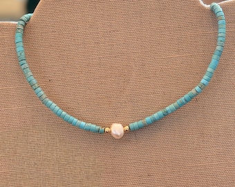 Può includere: Collana di perline turchesi con un singolo pendente di perla. La collana presenta piccole perline turchesi rotonde infilate con accenti color oro. La perla è di un morbido colore bianco sporco.