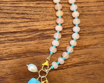 Può includere: Una delicata collana con perline bianche e color pesca, intervallate da perline turchesi. Una chiusura dorata tiene un ciondolo perlato, una pietra turchese con un piccolo cristallo e un ciondolo a lucchetto dorato.