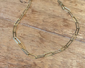 Può includere: Una collana a catena d'oro con un designo semplice e collegato. La catena è composta da piccoli anelli rettangolari.
