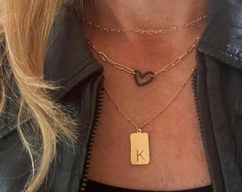 Può includere: Una collana dorata a più fili con un ciondolo a forma di cuore e un ciondolo rettangolare con la lettera 'K'.