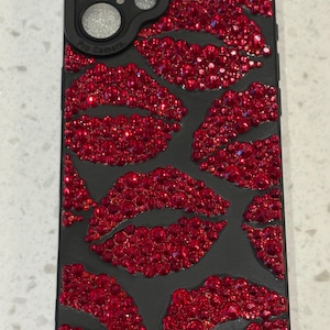 Peut inclure: Coque de téléphone noire ornée de plusieurs lèvres en cristal rouge. L'étui comporte un protecteur d'objectif d'appareil photo noir avec le texte "Pro Camera". Les lèvres sont faites de petits cristaux rouges scintillants.