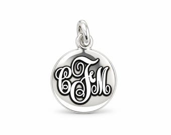 May include: A circular silver pendant featuring a polished metallic finish and a central black engraved monogram with the letters CFM in a decorative script font. The pendant includes a small silver jump ring at the top for attachment.