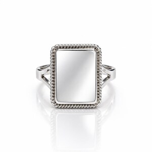May include: A silver-toned ring featuring a rectangular face with a smooth, reflective center panel. The rectangular centerpiece is framed by a textured, twisted rope-style border. The band of the ring splits into two sections.