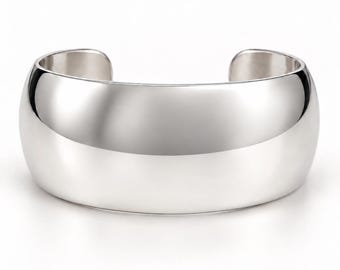 May include: A wide, polished silver cuff bracelet with a smooth, reflective surface and a curved, open-ended design. The metal has a bright, metallic finish that catches the light, creating soft highlights across the rounded, solid band structure.