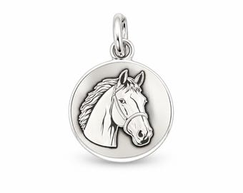 May include: A circular silver pendant featuring a detailed engraved profile of a horse head wearing a bridle. The design is centered on a smooth, polished disc with a raised border and a small silver jump ring attached to the top for hanging.