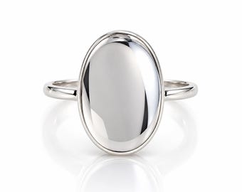 May include: A polished silver ring featuring a large, smooth, oval-shaped centerpiece. The metal surface is highly reflective, showing clear highlights and shadows. The band is thin, rounded, and connects to the oval setting at the sides.