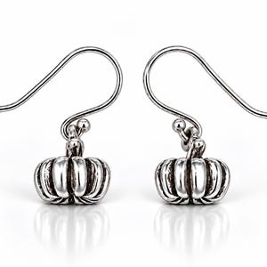 May include: A pair of silver-toned drop earrings featuring a small, three-dimensional pumpkin charm with vertical ridges and a polished finish. Each earring is attached to a curved ear wire hook, designed for hanging from the earlobe.