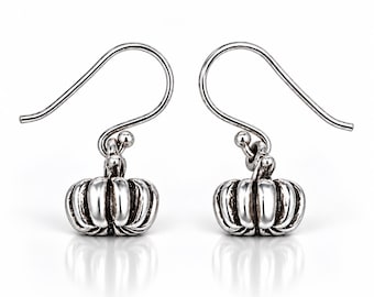 May include: A pair of silver-toned drop earrings featuring a small, three-dimensional pumpkin charm with vertical ridges and a polished finish. Each earring is attached to a curved ear wire hook, designed for hanging from the earlobe.