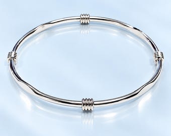 May include: A polished silver-tone bangle bracelet featuring a smooth, circular band. The design is accented with four evenly spaced, decorative stations, each consisting of a series of three small, raised horizontal ridges encircling the band.