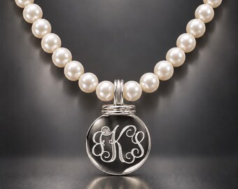 May include: A necklace featuring a strand of round, off-white pearls and a circular silver pendant. The pendant has a polished metallic finish and is engraved with a decorative, intertwined monogram featuring the letters B, K, and S in script.