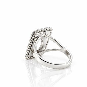 May include: A silver-toned ring featuring a rectangular face with a twisted rope-style border. The band is split into two thin, smooth arms that connect to the back of the rectangular setting, creating an open, airy structure.