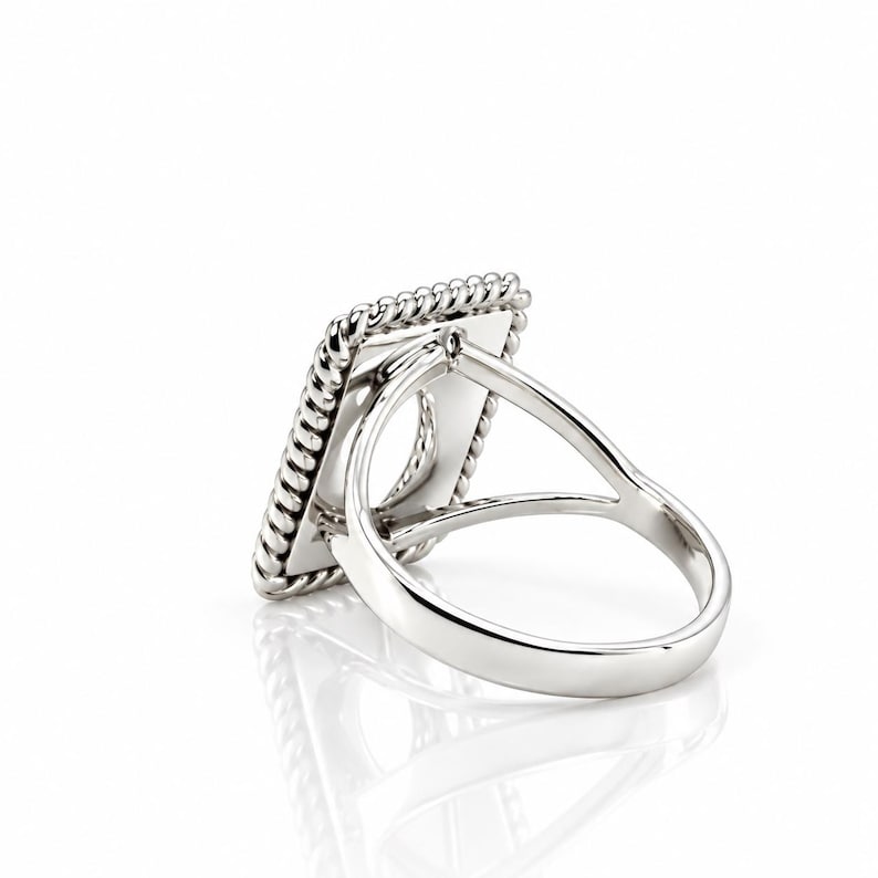 May include: A silver-toned ring featuring a rectangular face with a twisted rope-style border. The band is split into two thin, smooth arms that connect to the back of the rectangular setting, creating an open, airy structure.