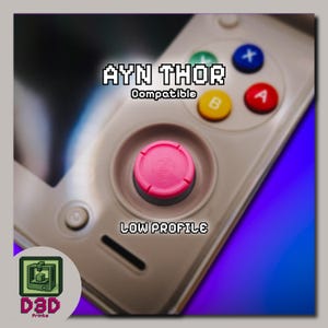 May include: A close-up of a gaming controller with a pink joystick and colorful buttons. The text "AYN THOR Compatible" and "LOW PROFILE" are displayed. A logo with the text "D3D Prints" is in the lower left corner.