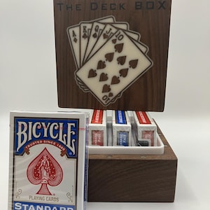 May include: A wooden deck box with the text "THE DECK BOX" and a display of playing cards. A Bicycle playing card deck is in front of the box. The box holds several decks of cards.