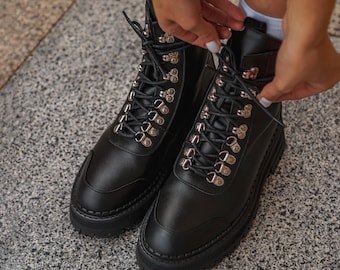 Botas de combate de cuero negro con ganchos de metal.
