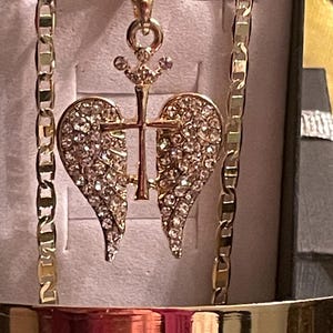 May include: Gold-coloured necklace with a pendant shaped like a heart, adorned with sparkling crystals. The pendant incorporates a cross and crown design. The chain is a classic link style. The jewellery is presented in a box.