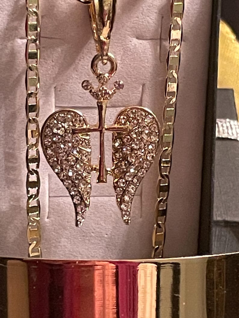 May include: Gold-coloured necklace with a pendant shaped like a heart, adorned with sparkling crystals. The pendant incorporates a cross and crown design. The chain is a classic link style. The jewellery is presented in a box.