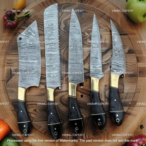 May include: A collection of six kitchen knives with patterned steel blades, brass bolsters, and black wooden handles. The knives are displayed on a wooden chopping board, with diverse blade shapes for various cooking needs.