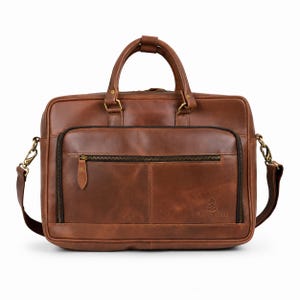 May include: A brown leather briefcase featuring two top handles, a detachable shoulder strap with brass-toned hardware, and a front zippered pocket. The bag displays the embossed text Chilgoza with a pinecone icon on the lower right corner.
