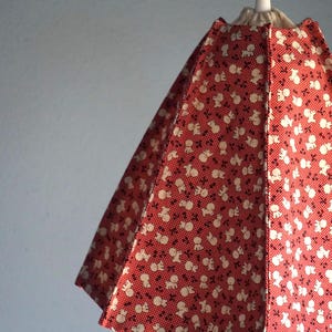 Puede incluir: Pantalla de lámpara roja y blanca con un patrón repetido de pequeñas figuras blancas sobre un fondo rojo. La pantalla cónica está suspendida de un cable blanco y parece ser de tela.