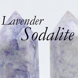 May include: Two lavender sodalite crystal towers. The crystals have a light purple and white color with a polished finish. The text "Lavender Sodalite" is written in black script across the top of the image.