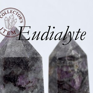 May include: Two Eudialyte crystal towers with a gray and purple marbled pattern. The crystals have a faceted top and are labeled "Collector's Item". The text "Eudialyte" is displayed in black.