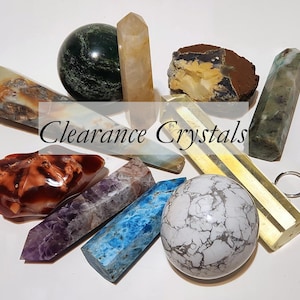 May include: A collection of various crystals and stones including spheres, points, and a raw slab. The items feature diverse colors like blue, purple, white, green, and brown. The text Clearance Crystals is overlaid in the center of the image.