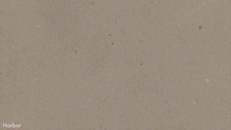 The image is a close-up of a textured surface, possibly a wall or a piece of paper, with a neutral beige color. There are small white specks scattered across the surface, adding some detail and contrast to the overall image.