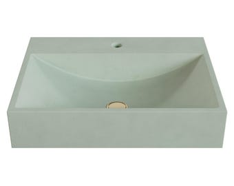 May include: A rectangular light sage green concrete bathroom sink with a smooth matte finish. The basin features a curved interior design, a single faucet hole located on the rear deck, and a circular metallic gold drain cover centered at the base.