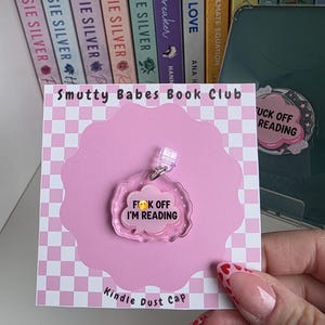 May include: A pink Kindle dust cap with the text "F*ck Off I'm Reading" and a pink cloud design. The cap is attached to a pink card with the text "Smutty Babes Book Club" and "Kindle Dust Cap".