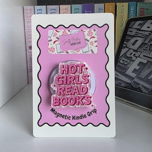 May include: A pink magnetic Kindle grip on a display card. The grip features the text HOT GIRLS READ BOOKS in a glittery pink font with a white outline. The display card includes the text Smutty Babes BOOK CLUB and Magnetic Kindle Grip.