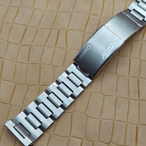 May include: A silver-toned stainless steel watch bracelet featuring a brushed metal finish. The folding clasp is engraved with the brand name SEIKO and the model name ACTUS. The link band consists of rectangular segments connected in a series.
