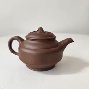 以下が含まれることがあります： 蓋と竹風の取っ手が付いた、小さな茶色のセラミックティーポット。 ティーポットには注ぎ口と丸みを帯びた本体があります。 色は豊かでアースカラーの茶色で、デザインはシンプルでエレガントです。 お茶を淹れるために。