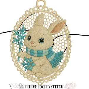 May include: Embroidered image of a rabbit wearing a blue and teal scarf, holding a snowflake. The rabbit is within a cream-coloured oval frame with a lace-like design. The text "THEVELOCITYSTITCH" is at the bottom.