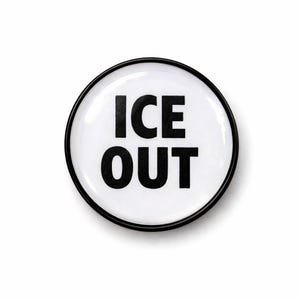 May include: A round, white button with a black border. The words "ICE OUT" are printed in bold, black capital letters in the center of the button. The button is set against a white background.