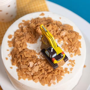 Bird eye view of the toy excavator take topper decor candle sitting on a birthday cake with cookie crumbs, construction themed soy wax birthday candle for boys and girls.
