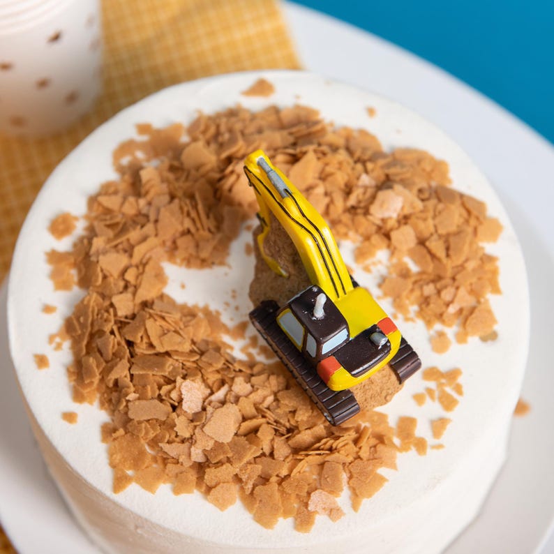 Bird eye view of the toy excavator take topper decor candle sitting on a birthday cake with cookie crumbs, construction themed soy wax birthday candle for boys and girls.