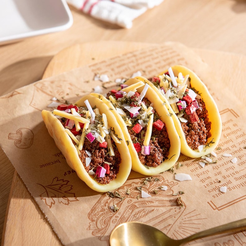 Close-up of realistic taco candles crafted from soy wax, featuring detailed shells filled with ground beef texture, shredded cheese wax melts, onions, and herbs. Handmade novelty food candle gift for taco lovers