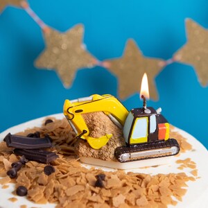 A closer look at the toy exvacator candle lit on fire sitting on a birthday cake as cake topper deocr construcrion themed candle.