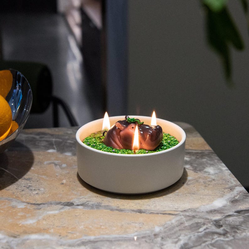 A glowing hippo candle bowl with three wicks lit creating a warm ambiance on a marble surface, a novelty animal candle décor piece ideal for gifting, relaxing, and adding cozy style to any modern home interior.