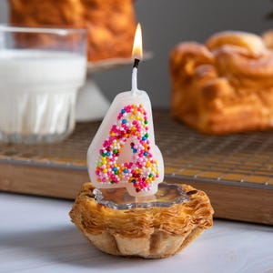 Burning sprinkles number 4 candle with rainbow sugar details, displayed as a novelty birthday cake decoration.