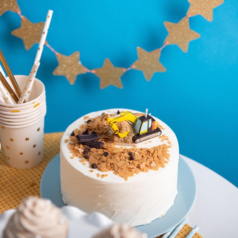 A futher view of the toy excavator cake tooper decoration construction themed party décor, handmade unscented soy wax candle for kids sitting on a full cake with a party setup background.