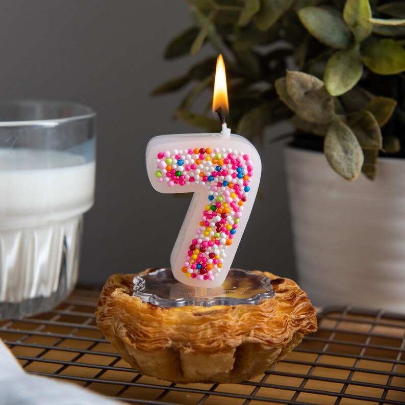 Number 7 birthday candle burning softly, decorated with colorful sprinkles and styled for a festive cake display.