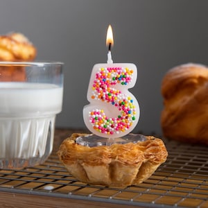 Hand-poured number 5 candy sprinkle candle lit and ready for cake topping, perfect for playful birthday celebrations.