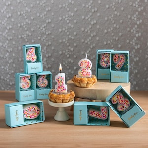 Sprinkles candy number candles displayed with light blue gift boxes packaging, featuring numbers 0–9 styled around pastries with number 1 and number 2 lit on small cakes, an unscented handmade birthday number candle collection designed for cake toppers and party celebrations.