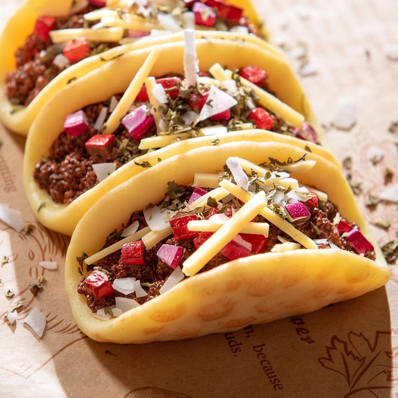 Macro close-up of hand-poured taco candles with realistic soy wax shells, ground beef texture, red onions, herbs, and shredded cheese wax melts. Unique novelty candle gift for taco lovers and perfect mexcian gift decoration candle birthday gifts.
