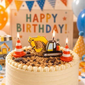 Toy excavator candle cake topper and traffic cone candle lit on a birthday cake, handmade soy wax construction themed cake decor for kids birthday parties, heavy equipment celebration candle with construction party backdrop and Happpy Birthday Banner.